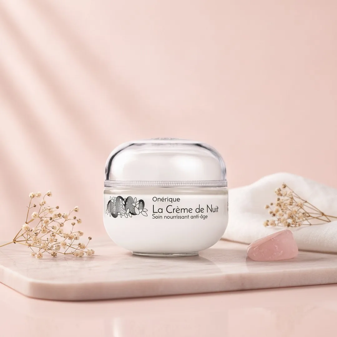 A frosted jar of night cream on pale pink stone with a rose-quartz roller and dried gypsophila.